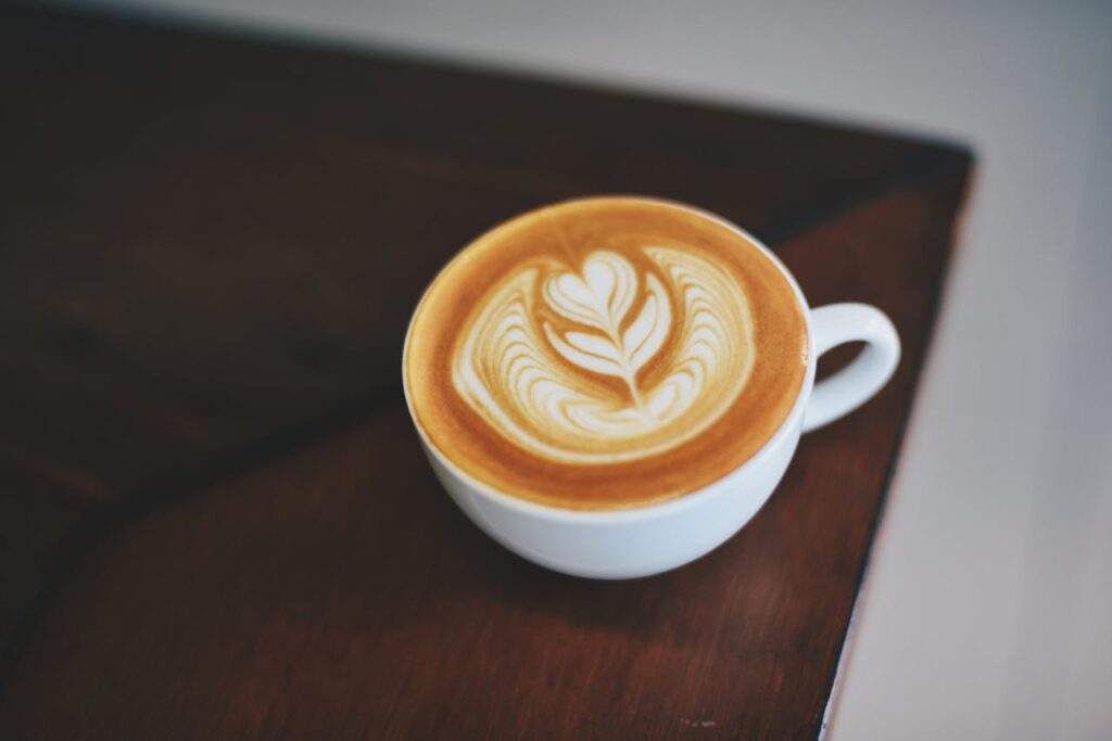 A beautifully crafted latte with intricate foam art in a white porcelain mug on a dark wooden table.